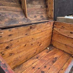 May include: An open, antique wooden chest with a weathered appearance. The chest is constructed from planks of wood, showing knots and variations in color. The interior is visible, revealing the chest's depth and construction. The wood has a warm, reddish-brown hue.