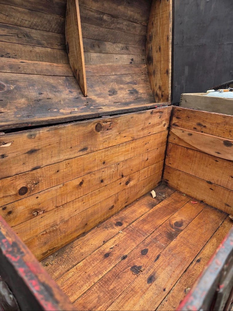 May include: An open, antique wooden chest with a weathered appearance. The chest is constructed from planks of wood, showing knots and variations in color. The interior is visible, revealing the chest's depth and construction. The wood has a warm, reddish-brown hue.