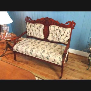 May include: A vintage loveseat with a dark wood frame and floral patterned upholstery. The backrest features a carved design, and the cushions are tufted. The fabric has a cream background with green and blue floral accents. The loveseat has a classic, antique style.