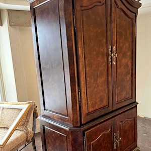 Puede incluir: Un gran mueble de madera marrón oscuro con detalles ornamentados. El mueble tiene dos puertas superiores y dos inferiores, todas con herrajes decorativos. El mueble se apoya en patas curvas con detalles dorados. La veta de la madera es visible.