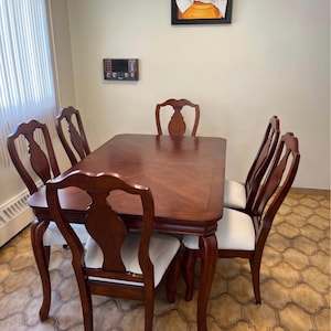 May include: A rectangular wooden dining table with a polished brown finish and a chevron-patterned top, accompanied by five matching chairs featuring curved backrests and white upholstered seats, arranged in a formal dining room setting.