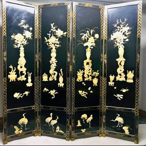 Peut inclure: Un paravent à quatre panneaux avec une finition laquée noire et des reliefs sculptés de couleur crème. Chaque panneau présente des compositions florales dans des vases, des créatures mythiques et des grues, encadrés par des bordures géométriques dorées.