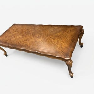 May include: A rectangular wooden coffee table featuring a rich brown wood grain pattern on the top surface, a scalloped edge design, and four curved legs that terminate in detailed feet with small black protective pads at the base.