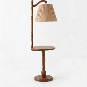 May include: A floor lamp with a round wooden side table integrated into its central post. The lamp features a dark brown wooden base and stand, topped with a beige pleated fabric lampshade that hangs from a curved arm extending from the post.