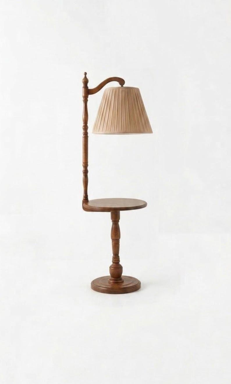 May include: A floor lamp with a round wooden side table integrated into its central post. The lamp features a dark brown wooden base and stand, topped with a beige pleated fabric lampshade that hangs from a curved arm extending from the post.