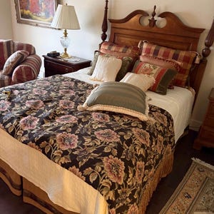 May include: A bedroom with a four-poster bed, featuring a dark floral patterned duvet cover and several decorative pillows. The bed has a wooden headboard and footboard. A fringed bed skirt and a patterned rug are also visible.
