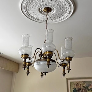 May include: An antique chandelier with five frosted glass shades and brass accents hangs from a white ceiling medallion. The chandelier has a central globe-shaped light fixture and curved arms.