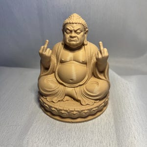 Può includere: Una statuetta monocromatica color beige chiaro raffigurante una figura seduta con la pancia rotonda, che indossa abiti tradizionali e mostra il dito medio con entrambe le mani. La figura ha un'acconciatura riccia e siede su una base a loto.