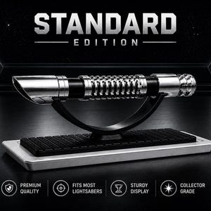 Pode incluir: Uma r&eacute;plica de sabre de luz prateado e preto, rotulada como "STANDARD EDITION", &eacute; exibida em um suporte preto com uma base prateada. O sabre de luz apresenta detalhes intrincados e foi projetado para caber na maioria dos sabres de luz. A imagem inclui &iacute;cones indicando qualidade premium e grau de colecionador.