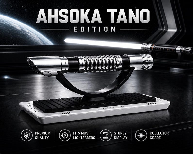 Pode incluir: Um sabre de luz prateado e preto com o texto "AHSOKA TANO EDITION" &eacute; exibido em um suporte preto. O sabre de luz est&aacute; em uma base branca com uma inser&ccedil;&atilde;o preta. A imagem tamb&eacute;m inclui um segundo sabre de luz no fundo.