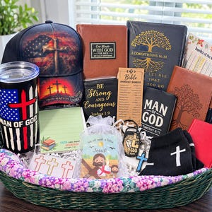 May include: A gift basket containing a black baseball cap with a cross and American flag, a black tumbler with a cross, several books including One Minute With God, a Bible emergency numbers card, a Man of God journal, a keychain, and black socks.