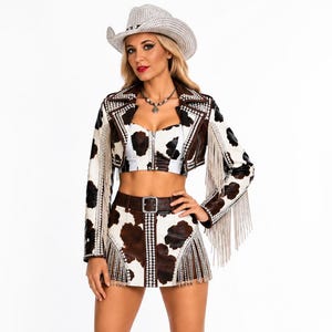 May include: A cow-print outfit featuring a cropped jacket with long fringe and silver studs, a matching zip-front bustier top, and a mini skirt with a belt and fringe trim. The ensemble includes a silver-studded cowboy hat and brown leather boots.