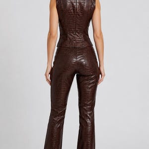 May include: A dark brown sleeveless vest and matching long trousers set featuring a textured crocodile skin pattern. The vest has a fitted silhouette with a back zipper closure, and the trousers are straight-legged with a high-waisted design.