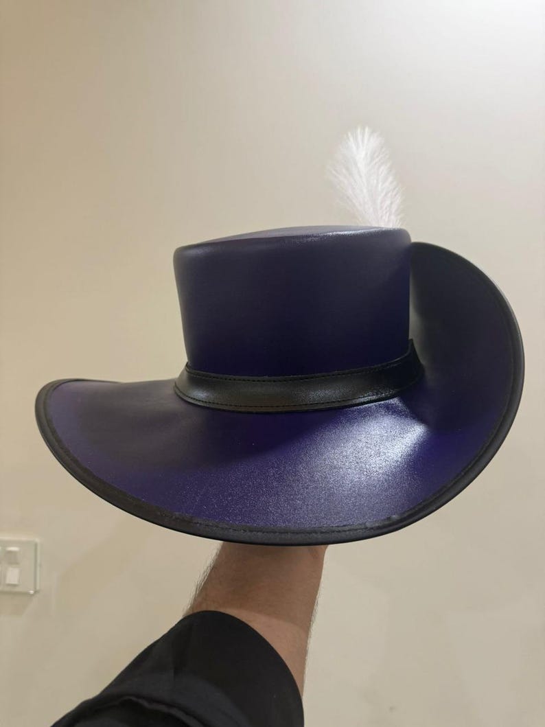 May include: A dark blue, wide-brimmed hat with a black band and a single white feather. The hat has a cylindrical crown and a broad, curved brim. The hat is held up against a neutral background.