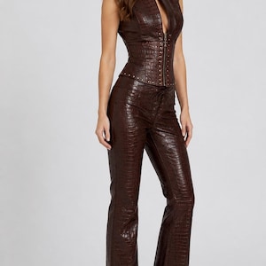 May include: A dark brown sleeveless top and matching trousers set featuring a textured crocodile-embossed pattern. The top has a front zipper closure and metallic stud detailing along the hem, while the trousers feature a lace-up front closure.
