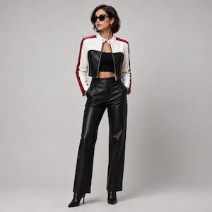 May include: A cropped jacket featuring a white torso, black lower panels, and red sleeve stripes, worn over a black crop top. The outfit includes high-waisted black trousers with a straight-leg cut and black pointed-toe boots, paired with dark sunglasses.