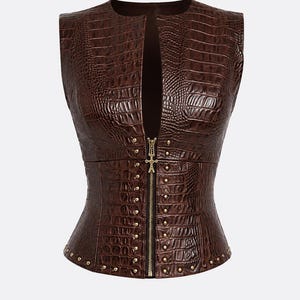 May include: A sleeveless brown vest featuring a textured crocodile skin pattern. The garment has a deep front opening secured by a central gold-toned zipper with a decorative pull, accented by small gold-toned studs along the front and hem.
