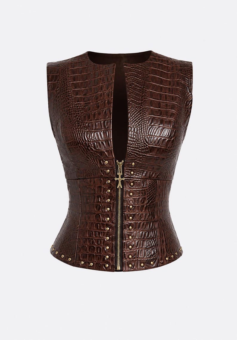 May include: A sleeveless brown vest featuring a textured crocodile skin pattern. The garment has a deep front opening secured by a central gold-toned zipper with a decorative pull, accented by small gold-toned studs along the front and hem.