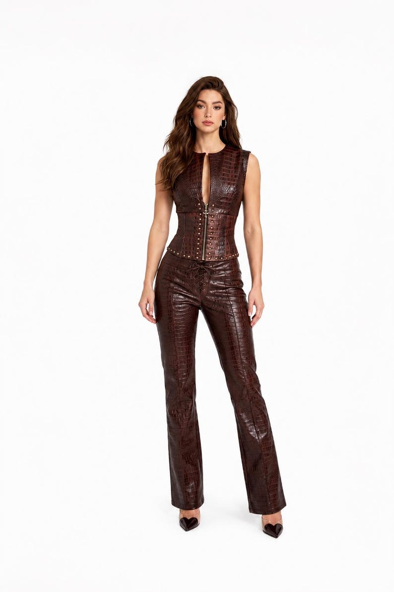 May include: A dark brown sleeveless top and matching trousers set featuring a textured crocodile skin pattern. The top has a front zipper closure and metallic stud detailing along the waist, while the trousers feature a lace-up front design.