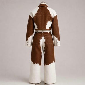 May include: A two-piece set consisting of a cropped jacket and high-waisted wide-leg trousers, both featuring a brown and white cow-print pattern. The jacket has a collar and long sleeves, while the trousers include a matching belt at the waist.