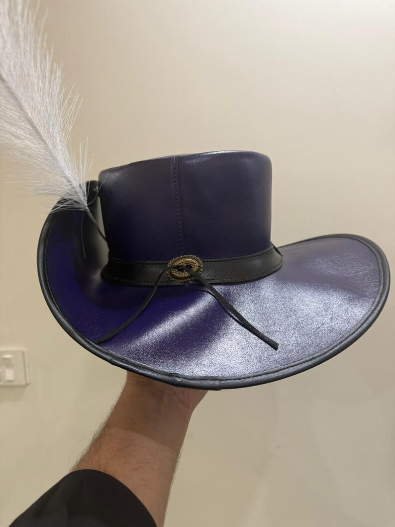 May include: A dark purple hat with a wide brim and a tall crown. The hat features a black band with a decorative buckle and a white feather. The hat is made of a shiny material and has a classic design.