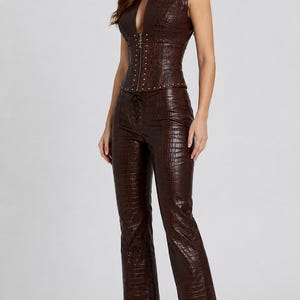 May include: A dark brown sleeveless top and matching trousers set featuring a textured crocodile-embossed pattern. The top has a front zipper closure with metallic stud detailing, while the trousers include a lace-up front closure detail.