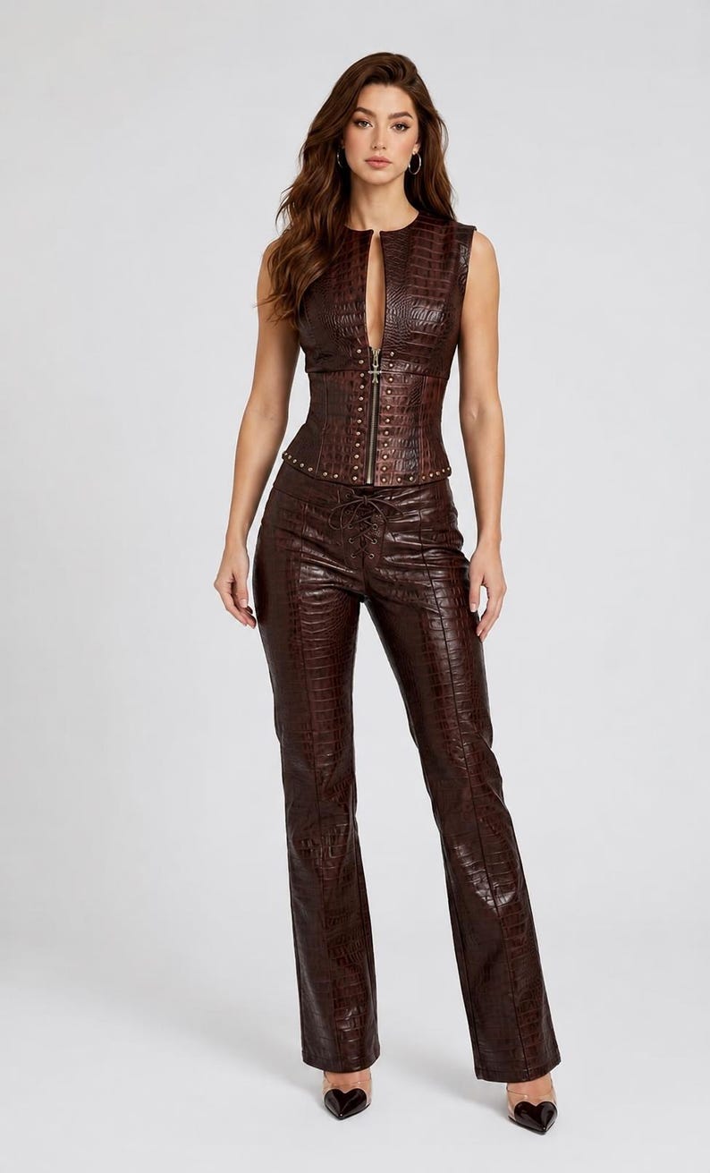 May include: A dark brown sleeveless corset top and matching trousers set featuring a textured crocodile skin pattern. The corset top has a front zipper closure with metallic stud detailing along the hem, while the trousers feature a lace-up front.