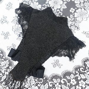 K&ouml;nnte beinhalten: Schwarzer, mit Perlen besetzter Schal mit floralen Mustern und Fransen. Der Schal hat eine zarte Spitzenborte und Schleifenb&auml;nder. Das aufwendige Design und die dunkle Farbe erzeugen eine elegante und Vintage-&Auml;sthetik.