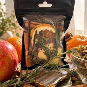 May include: A black resealable pouch containing a mixture of dried orange slices, cinnamon sticks, and sprigs of rosemary. The clear front window displays the botanical ingredients, which are intended for simmering or decorative use.