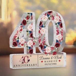 Könnte beinhalten: Klare Acryl-Dekoration zum 40. Jahrestag. Die Zahlen sind mit einem Blumendesign aus roten, rosa und blauen Blumen gefüllt. Die Basis trägt die Aufschrift "40th Anniversary" und die Namen "Donna & Nick" mit dem Hochzeitsdatum.