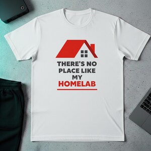 Puede incluir: Camiseta blanca con un gráfico de una casa roja y el texto "THERE'S NO PLACE LIKE MY HOMELAB" en negro y rojo. La camiseta está hecha de un material suave y tiene cuello redondo.