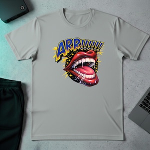 May include: A light gray t-shirt featuring a graphic of open red lips with white teeth and a long pink tongue. The word "ARR!!!!!!" is written above the lips in blue and yellow. The shirt is made of a soft material.