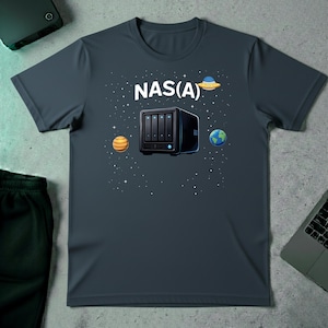 Op de afbeelding: Donkergrijs t-shirt met de tekst "NAS(A)" en een afbeelding van een NAS-apparaat, planeten en een ruimteschip. Het ontwerp is gedrukt op een t-shirt met korte mouwen en een ronde hals.