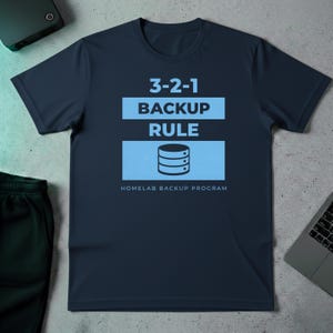 Op de afbeelding: Marineblauw t-shirt met de tekst "3-2-1 BACKUP RULE" in wit en lichtblauw. Daaronder een lichtblauwe rechthoek met een serverafbeelding. De woorden "HOMELAB BACKUP PROGRAM" staan eronder.