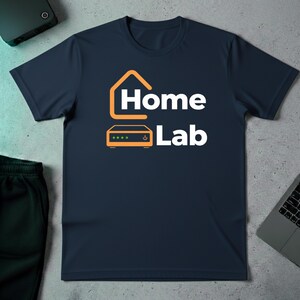Puede incluir: Camiseta azul marino con la frase "Home Lab" en blanco y un gráfico naranja de una casa y un router. La camiseta está hecha de un material suave y es adecuada para uso casual.