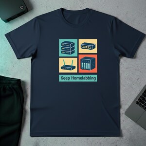 Może przedstawiać: Granatowa koszulka z grafiką urządzeń sieciowych w kolorowych kwadratach. Projekt zawiera stos serwerów, przełącznik, router i urządzenie NAS. Tekst "Keep Homelabbing" znajduje się poniżej.