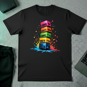 May include: Black t-shirt featuring a colorful graphic of stacked, retro-style electronic devices. The devices are in pink, orange, green, yellow, and blue, with a splash of paint behind them. The design is vibrant and eye-catching.