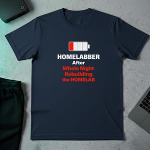 May include: Navy blue t-shirt with the text "HOMELABBER After Whole Night Rebuilding the HOMELAB" and a battery icon. The battery icon shows a low charge. The shirt is a casual wear item.