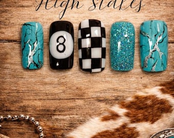 May include: Five artificial nails with diverse designs: turquoise marble, an eight ball, a black and white checkerboard, teal glitter, and turquoise marble with silver accents. The cursive text reads "High Stakes".
