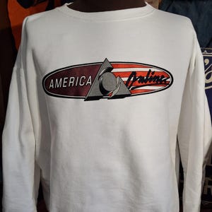 May include: White sweatshirt with long sleeves. The front features a graphic with the words "AMERICA Online" in a red, orange, and gray design. The sweatshirt is displayed on a mannequin.