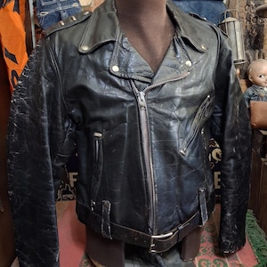 May include: A black leather motorcycle jacket featuring a wide notched collar, an asymmetrical silver-tone metal zipper closure, zippered pockets, shoulder epaulets with metal snaps, and an adjustable waist belt with a silver-tone metal buckle.