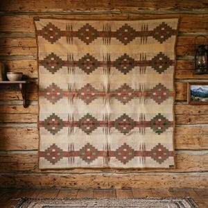 May include: A rectangular woven blanket featuring a repeating geometric pattern of dark brown, olive green, and rust red diamonds arranged in horizontal bands against a cream-colored background, finished with a solid brown fabric border.