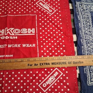 K&ouml;nnte beinhalten: Rote und wei&szlig;e Bandanas mit Polka-Dots, dem OshKosh B'Gosh-Logo und Text. Ein Holzlineal liegt &uuml;ber den Bandanas. Die Bandanas bestehen aus 100 % Baumwolle.