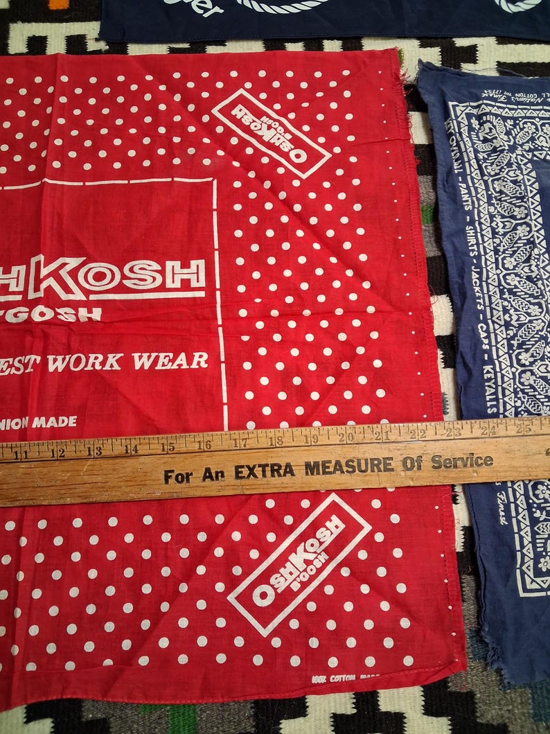 K&ouml;nnte beinhalten: Rote und wei&szlig;e Bandanas mit Polka-Dots, dem OshKosh B'Gosh-Logo und Text. Ein Holzlineal liegt &uuml;ber den Bandanas. Die Bandanas bestehen aus 100 % Baumwolle.