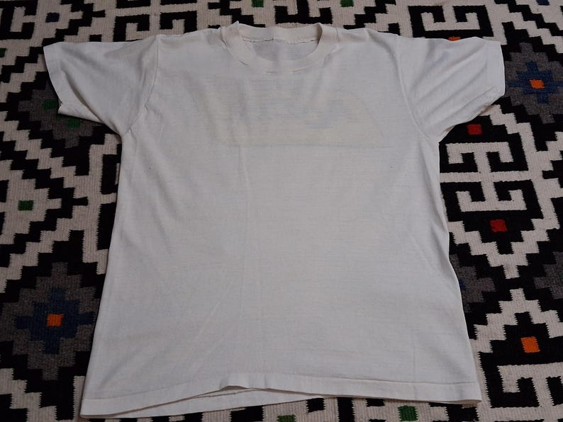 K&ouml;nnte beinhalten: Ein schlichtes wei&szlig;es T-Shirt mit kurzen &Auml;rmeln, flach hingelegt. Das Shirt besteht aus einem weichen, wahrscheinlich Baumwollmaterial. Der Kragen ist ein einfacher Rundhalsausschnitt. Das Shirt ist sauber und scheint ungetragen zu sein.