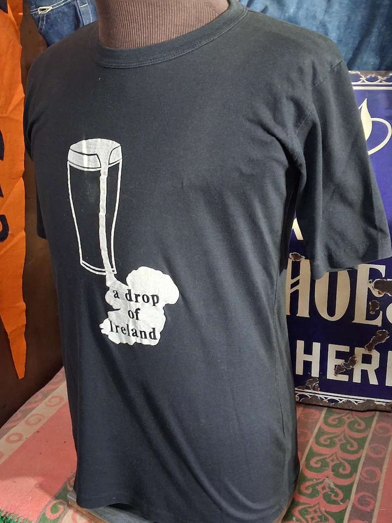 Op de afbeelding: Donkergrijs t-shirt met een witte afbeelding van een pint bier en de tekst "a drop of Ireland". Het shirt heeft een ronde hals en korte mouwen. Het shirt wordt op een mannequin getoond.