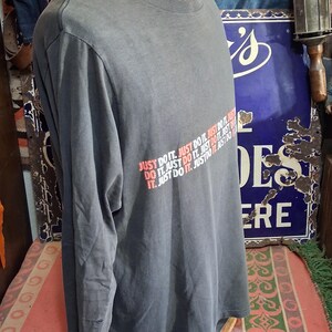 Puede incluir: Una camiseta gris de manga larga con el texto "JUST DO IT" en rojo y blanco. La camiseta se muestra en un maniqu&iacute;. La camiseta es de estilo casual.