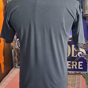 Op de afbeelding: Een donkergrijs t-shirt met korte mouwen. Het shirt is gemaakt van een zacht materiaal en heeft een ronde hals. De achterkant van het shirt is zichtbaar, met het eenvoudige ontwerp en de pasvorm. Het shirt wordt op een mannequin getoond.