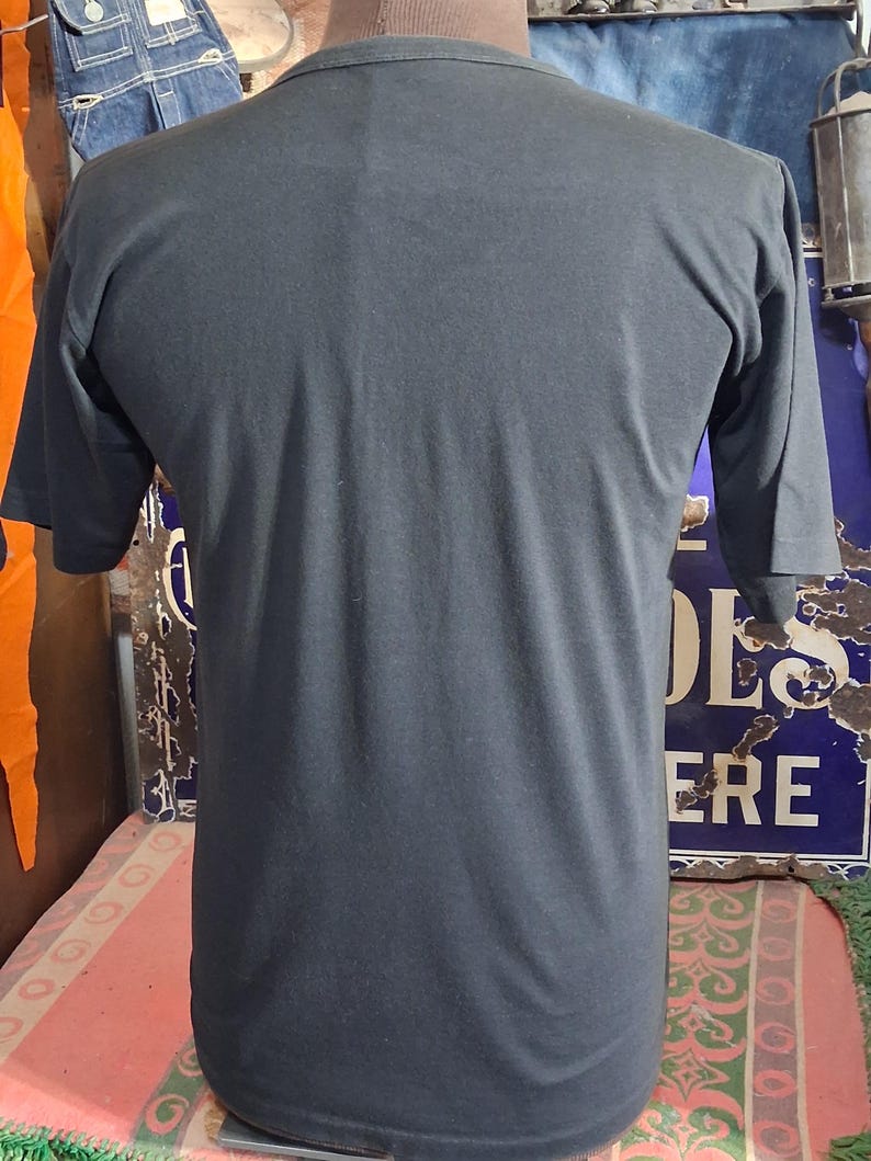 Op de afbeelding: Een donkergrijs t-shirt met korte mouwen. Het shirt is gemaakt van een zacht materiaal en heeft een ronde hals. De achterkant van het shirt is zichtbaar, met het eenvoudige ontwerp en de pasvorm. Het shirt wordt op een mannequin getoond.