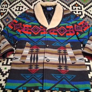 May include: A wool coat with a colorful geometric pattern in shades of blue, green, red, and brown. The coat has a cream-colored shearling collar, two front pockets, and two buttons. The sleeves have a unique patterned design.